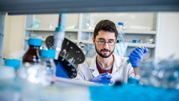 Male student wearing glasses, a lab coat and gloves doing something scientific.